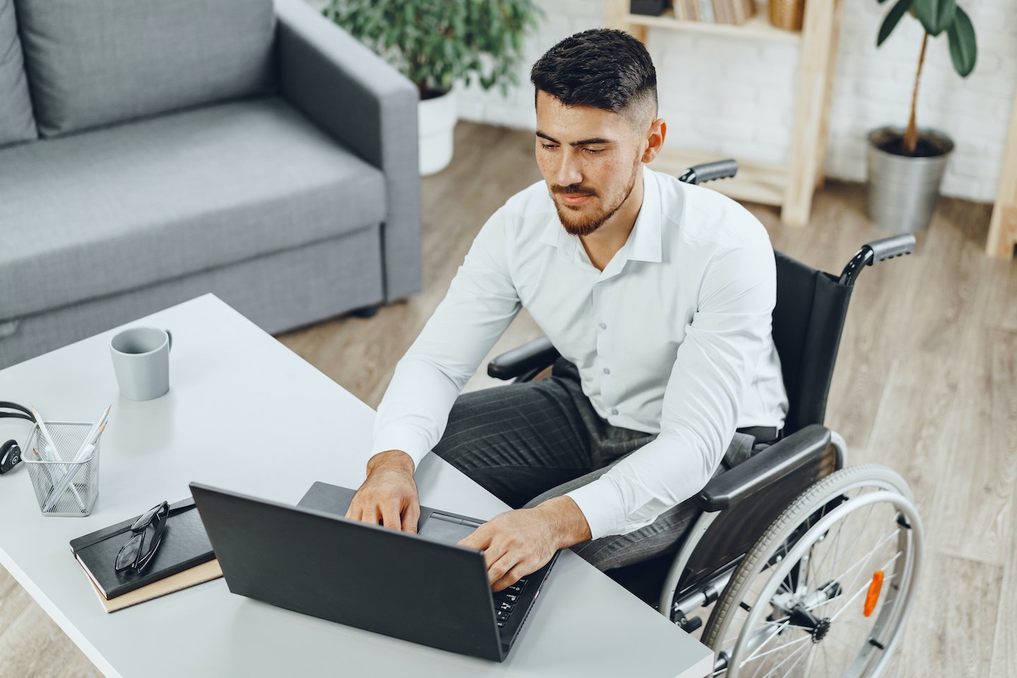 Disabled young man in wheelchair working in office with laptop