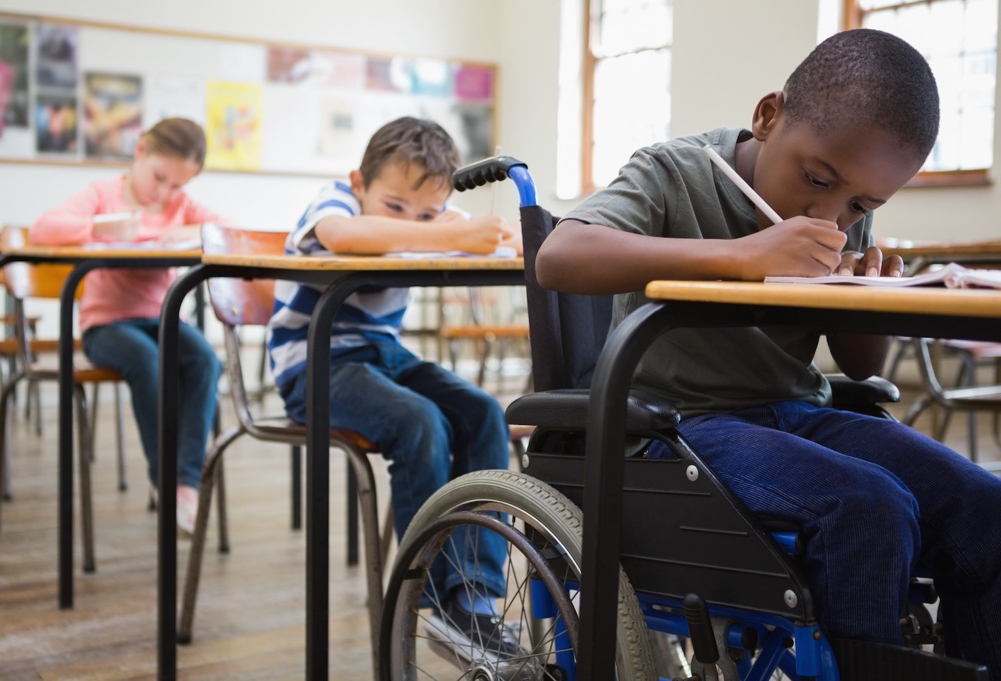 Boy in wheelchair doing schoolwork at his desk.