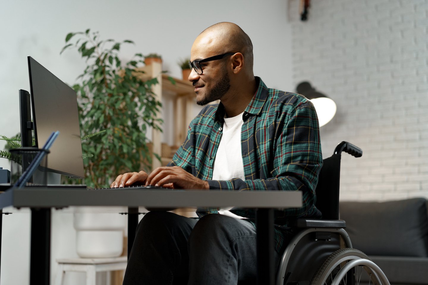 Disabled young african american man in wheelchair using computer while sitting at his working table close up
