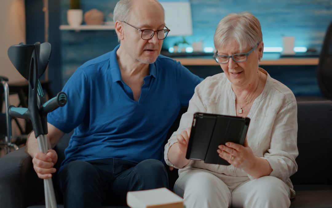 Elderly couple sitting on a couch, looking at the screen of an iPad